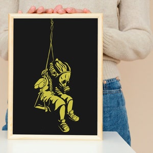 May include: A framed art print featuring a yellow silhouette of a child wearing a gas mask on a swing against a black background. The artwork has a minimalist style with a wooden frame.