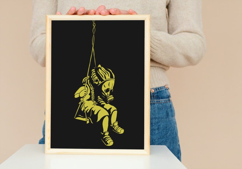 May include: A framed art print featuring a yellow silhouette of a child wearing a gas mask on a swing against a black background. The artwork has a minimalist style with a wooden frame.