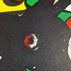 May include: Abstract artwork with a textured black background. The design features bold shapes in red, white, green, yellow, and blue. A prominent red and white circular shape is visible.
