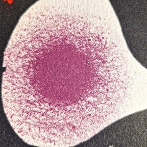 May include: Abstract artwork featuring a white, teardrop-shaped form with a central burst of magenta spray paint. The magenta color fades outwards, contrasting with the white background and a surrounding black area. The image has a textured appearance.