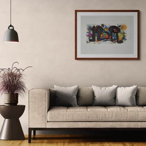 May include: Abstract art print in a dark wood frame. The artwork features a colorful, abstract design with black, blue, orange, and yellow shapes. The print is mounted on a white background and hangs above a beige sofa.