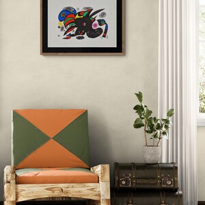 May include: Abstract art print in a wooden frame. The artwork features a black figure with colorful accents of red, blue, green, and yellow. A wooden chair with orange and green cushions is in the foreground, with a stack of dark brown vintage suitcases.