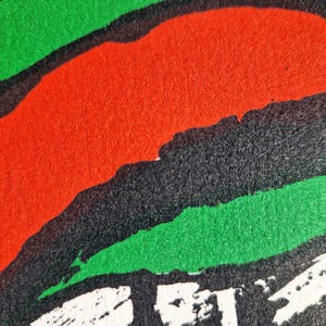 May include: Abstract design with bold strokes of red, green, and black. The image features a textured surface with a dynamic composition of overlapping shapes. White brushstrokes are visible at the bottom. The artwork has a modern, graphic feel.