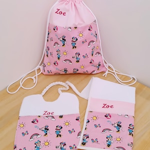 Può includere: Un set rosa composto da zaino con coulisse, bavaglino e asciugamano. Il set presenta un motivo a righe rosa e bianche con Minnie Mouse, arcobaleni e soli. Il nome "Zoe" è ricamato su ogni articolo.