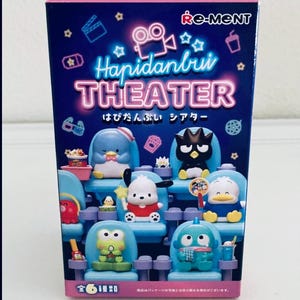 May include: A colorful box featuring the text "Hapidanbui THEATER" with Japanese text below. The box displays cartoon characters seated in theater chairs. The box is primarily blue, pink, and white.
