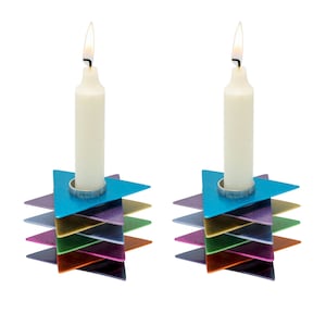 May include: Two white candles are lit in a colorful, layered, star-shaped menorah. The menorah is made of metal and has a blue, purple, green, orange, pink, and red color scheme.