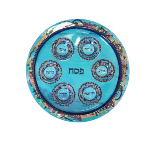 May include: A blue Passover Seder plate with a colorful city scene border. The plate has six sections with Hebrew text, including "Pesach" in the center.