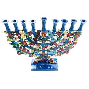 Op de afbeelding: Een blauwe menora met negen kaarshouders. De menora is versierd met kleurrijke vogels, bloemen en bladeren. De basis is rechthoekig en blauw geschilderd. Het ontwerp is ingewikkeld en gedetailleerd.