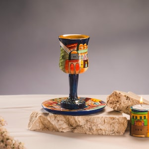 Könnte beinhalten: Eine handbemalte Keramik-Kiddusch-Schale mit einem farbenfrohen Stadtbild-Design, ein passender Teller und ein kleiner Kerzenhalter mit ähnlichem Design.