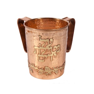 Puede incluir: Una copa de Kiddush de cobre martillado con dos asas y una inscripción dorada de las palabras hebreas "L'chaim" y un borde decorativo de granadas.