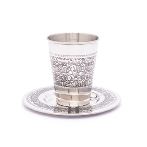 Puede incluir: Una copa de Kiddush de plata y un plato a juego con un diseño intrincado de un horizonte de ciudad. La copa y el plato están decorados con un patrón repetitivo de edificios y arcos.