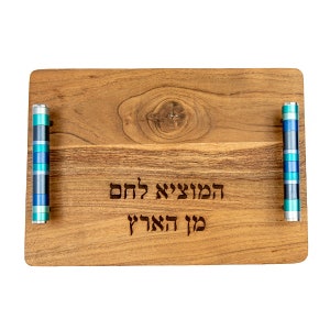 Puede incluir: Una bandeja de servir de madera con asas rayadas azules y verdes. La bandeja tiene el texto hebreo "La alegr&iacute;a de la vida est&aacute; en dar" grabado en ella.