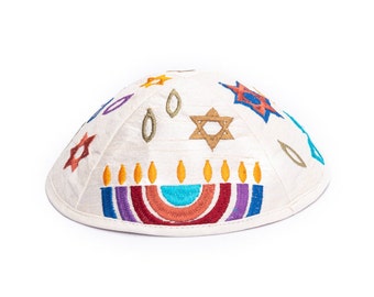 Può includere: Kippah bianca con ricamo colorato di una menorah, stelle di David e altri simboli ebraici.