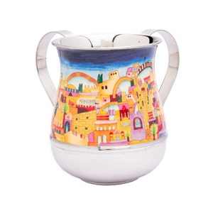 Könnte beinhalten: Eine silberfarbene Tasse mit zwei Henkeln, die eine farbenfrohe, gemalte Szene einer Stadt mit Gebäuden in Gelb-, Orange-, Rosa- und Lilatönen zeigt. Der Himmel ist blau. Die Tasse hat einen abgerundeten Boden.