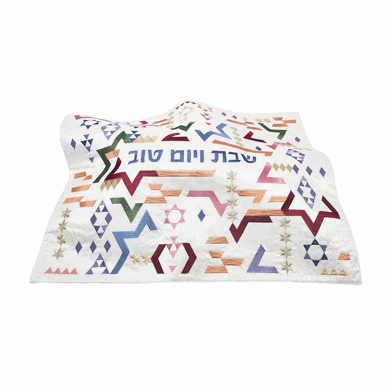 May include: White embroidered fabric with a geometric pattern in shades of blue, green, pink, red, and orange. The fabric has the Hebrew text "Shabbat Shalom" in the center.