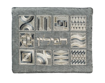 May include: A gray fabric prayer shawl with a geometric pattern and the Hebrew word "Hakadosh" embroidered in gold thread.