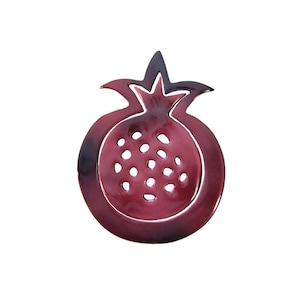May include: A ceramic pomegranate-shaped dish with a red glaze and a black outline. The dish has a cutout design of pomegranate seeds.