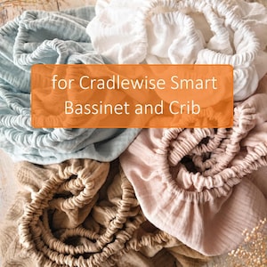 May include: A selection of soft, gathered cot sheets in shades of light blue, white, tan, and pink. The sheets, made from a textured fabric, are designed for a Cradlewise Smart Bassinet and Crib.