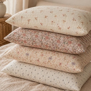 Könnte beinhalten: Ein Stapel aus vier rechteckigen Kissen mit verschiedenen Blumenmustern auf strukturiertem, cremefarbenem Stoff. Jedes Kissen zeigt einen einzigartigen Druck mit kleinen botanischen Motiven in gedeckten Rosa-, Braun-, Blau- und Grüntönen.