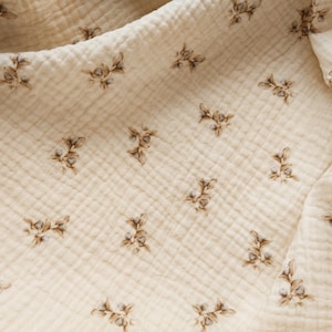 Puede incluir: Primer plano de una tela de color crema con un sutil estampado floral. La tela tiene una textura similar a un waffle.