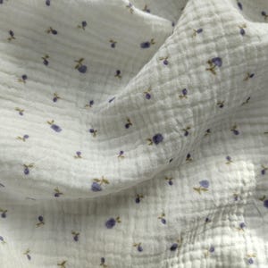 May include: White muslin fabric with a repeating pattern of small purple berries and brown stems. The fabric has a crinkled texture and is slightly translucent, with shadows adding depth to the image.