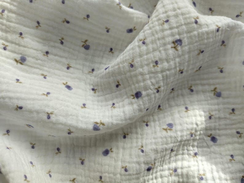 May include: White muslin fabric with a repeating pattern of small purple berries and brown stems. The fabric has a crinkled texture and is slightly translucent, with shadows adding depth to the image.