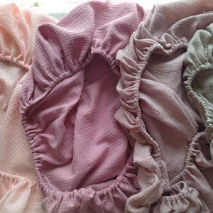 It shows fitted crib sheets made of organic muslin cotton. Perfect for baby oval or bedside cribs, bassinets and cradle. It's cozy pastel baby nursery, ideal for all Stokke cribs.