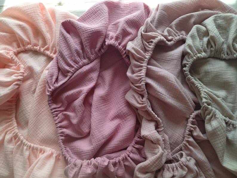 It shows fitted crib sheets made of organic muslin cotton. Perfect for baby oval or bedside cribs, bassinets and cradle. It's cozy pastel baby nursery, ideal for all Stokke cribs.