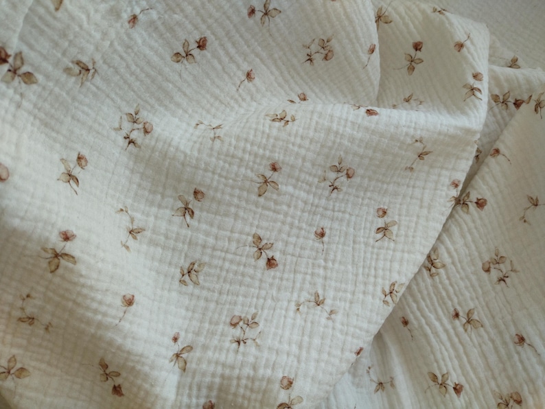 Puede incluir: Tela blanca con un peque&ntilde;o estampado floral marr&oacute;n. La tela tiene una textura similar a una gofre.