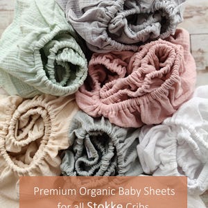 It shows fitted crib sheets made of organic muslin cotton. Perfect for baby oval or bedside cribs, bassinets and cradle. It's cozy pastel baby nursery, ideal for all Stokke cribs.