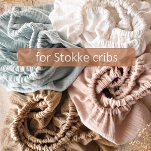 It shows fitted crib sheets made of organic muslin cotton. Perfect for baby oval or bedside cribs, bassinets and cradle. It's cozy pastel baby nursery, ideal for all Stokke cribs.