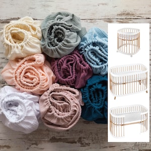 Peut inclure: Divers draps-housses pour berceau aux couleurs variées, crème, pêche et turquoise, sont disposés sur une surface en bois. L'image présente également un lit bébé ovale blanc et bois en trois vues, mettant en valeur le design.