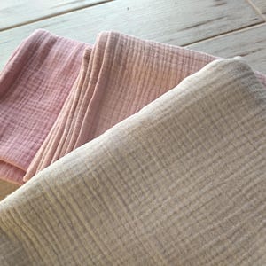 May include: Two folded pieces of fabric, one pink and one beige, with a textured woven pattern. The fabric is soft and lightweight.