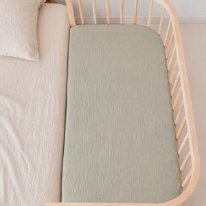 It shows fitted crib sheets made of organic muslin cotton. Perfect for baby oval or bedside cribs, bassinets and cradle. It's cozy pastel baby nursery, ideal for all BabyBay bedside cribs.