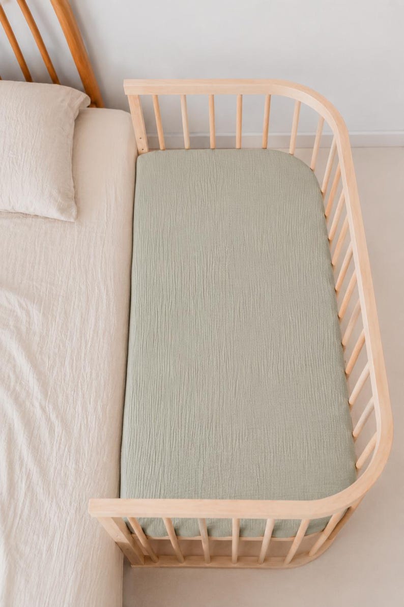 It shows fitted crib sheets made of organic muslin cotton. Perfect for baby oval or bedside cribs, bassinets and cradle. It's cozy pastel baby nursery, ideal for all BabyBay bedside cribs.