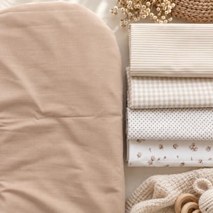 Peut inclure: Une pile de quatre pièces de tissu pliées comprenant un tissu beige uni, un tissu à rayures beige et blanc, un tissu à carreaux vichy beige et blanc, et un tissu blanc à pois beiges et à petits motifs floraux, le tout soigneusement disposé.