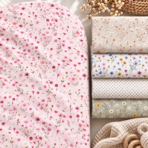 Op de afbeelding: Een groot stuk roze stof met een delicaat bloemenpatroon met kleine rode en roze bloemen, weergegeven naast een stapel van vier gevouwen stoffen vierkanten in beige, wit en groen met diverse bloemen- en stippenpatronen.