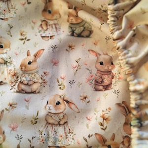 Pode incluir: Um tecido de cor creme com um padrão repetitivo de coelhos ilustrados em várias roupas, incluindo vestidos florais e camisolas, intercalados com pequenas flores silvestres cor-de-rosa e laranja e folhagem verde, com uma borda franzida.