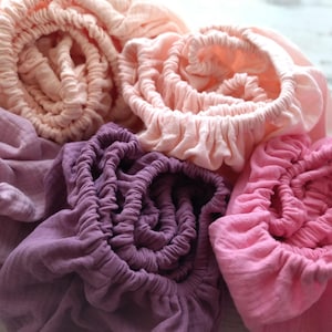 May include: A collection of five gathered fabric pieces in various shades of pink and purple. The textiles feature a crinkled texture and elasticized edges, creating a soft, layered appearance with colors ranging from pale peach to deep magenta.