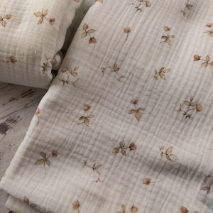 Puede incluir: Una tela de muselina blanca con un delicado estampado floral en tonos marrones. La tela tiene una superficie suave y texturizada y es perfecta para proyectos de artesan&iacute;a o costura.