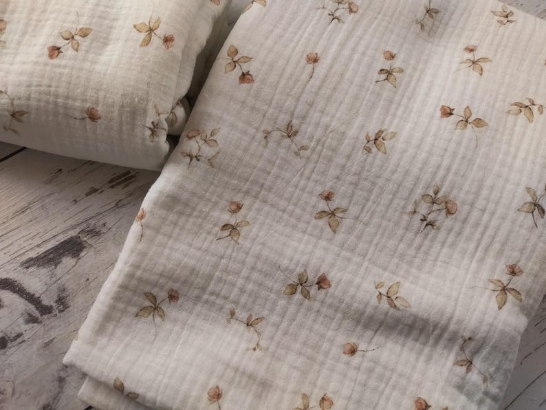 Puede incluir: Una tela de muselina blanca con un delicado estampado floral en tonos marrones. La tela tiene una superficie suave y texturizada y es perfecta para proyectos de artesan&iacute;a o costura.