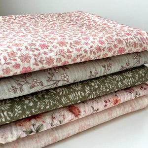 Puede incluir: Una pila de cinco piezas de tela con estampados florales. La pieza superior tiene un fondo blanco con pequeñas flores rosas. Las otras piezas tienen diseños florales variados en tonos verdes, rosas y marrones. Las telas parecen suaves y ligeras.