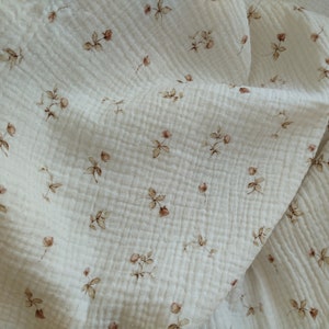 May include: Off-white muslin fabric with a delicate floral pattern. The fabric features small, brown rose illustrations scattered across its surface. The material has a textured, crinkled appearance, suggesting a soft and breathable quality.
