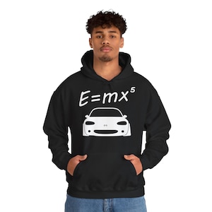 Puede incluir: Sudadera con capucha negra con un gráfico blanco de un coche y la ecuación E=mx⁵. El gráfico del coche es una vista frontal estilizada. La sudadera tiene un bolsillo delantero y una capucha con cordón.