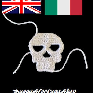 May include: White crocheted skull with eye holes. The skull is hanging from two white strings.