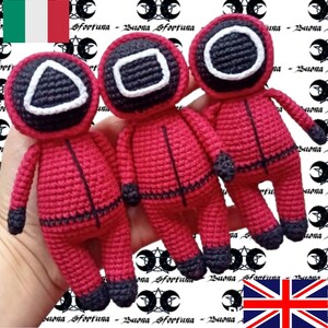 Può includere: Tre figure rosse all'uncinetto con contorni neri e volti bianchi di forme diverse. Le figure sono in piedi su una mano.