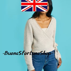May include: A white knitted wrap cardigan with a V-neck and long sleeves. The cardigan has a tie at the waist and is made of a soft, textured fabric. The text "BuonasfortunaShop" is visible at the bottom of the image.