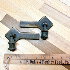 May include: Two antique brass cabinet door pulls with a diamond-shaped plate and a round knob. The pulls are approximately 4 inches long and are made in the USA.