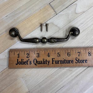 May include: Antique brass cabinet pull with a decorative design. The pull is 4 inches long and comes with two screws.