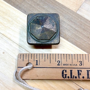 May include: A square-shaped brass cabinet knob with a faceted design. The knob measures approximately 1 inch in diameter.